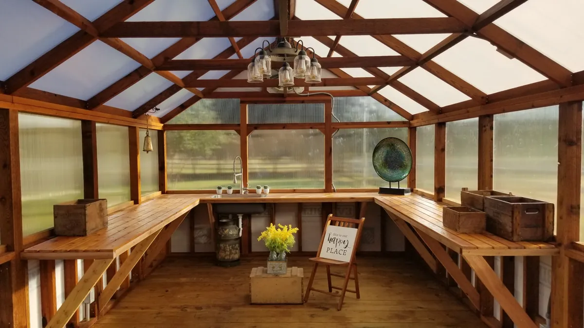 Inside a cedar greenhouse with wraparound cedar potting benches, a utility sink, a light fixture, and a wood floor