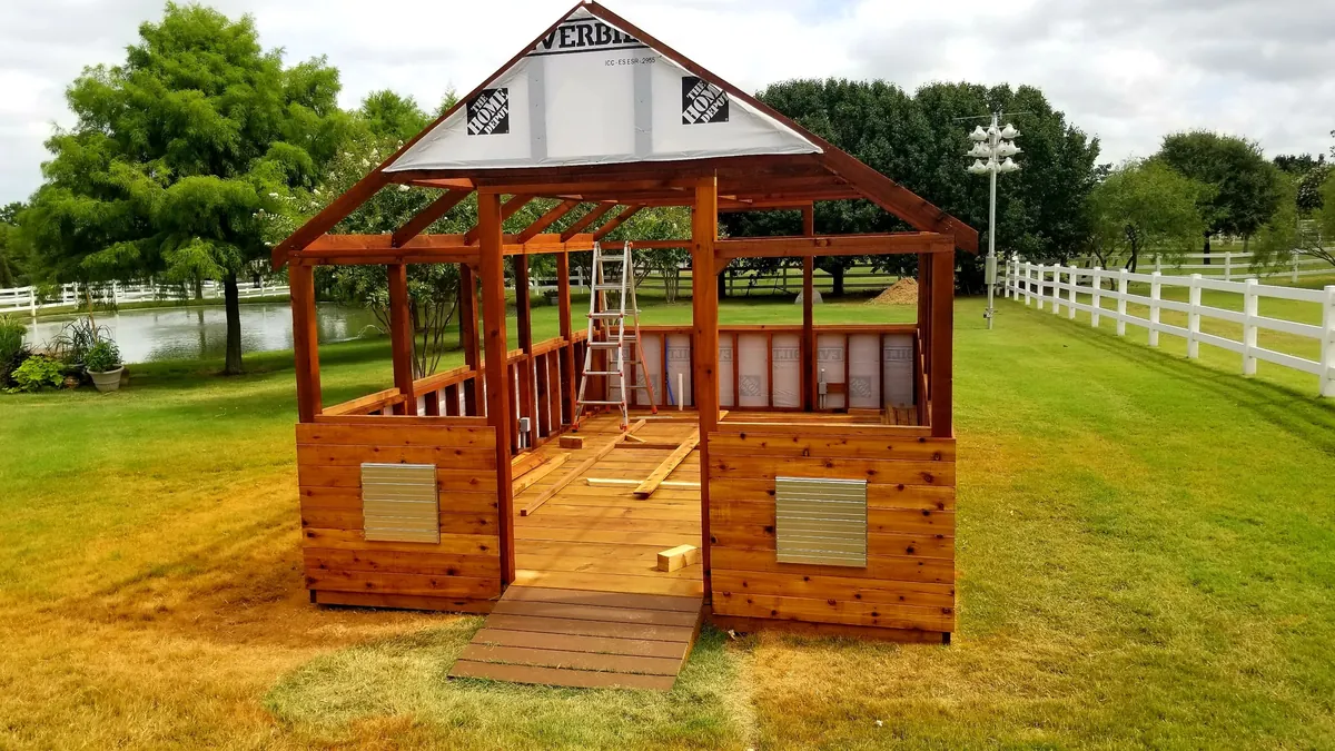 Cedar greenhouse during construction with the cedar knee wall, louvered vents, and roof framing complete