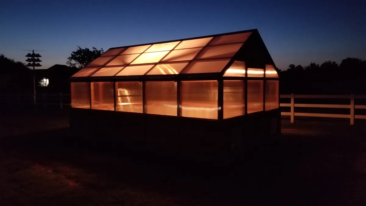 Custom greenhouse glowing at dusk with interior lights on through polycarbonate panels
