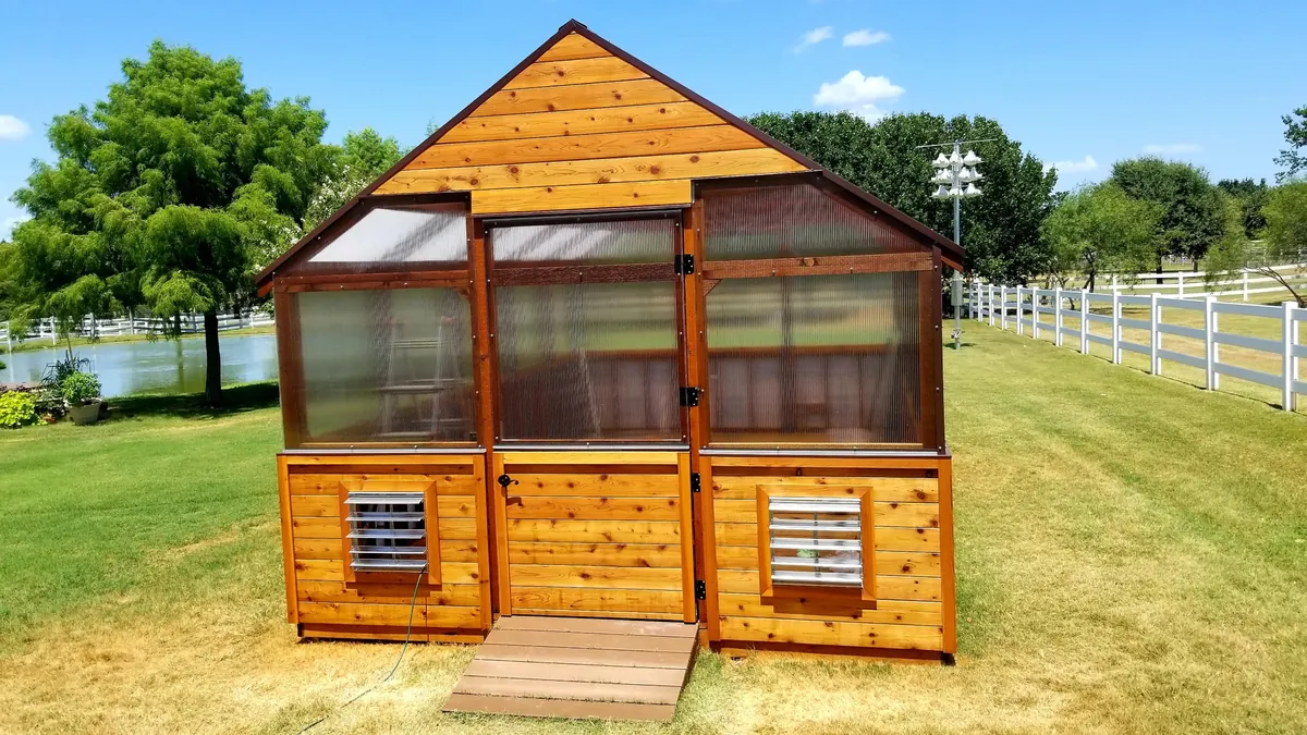 Front of a custom cedar greenhouse with a cedar door, polycarbonate panels, and louvered vents