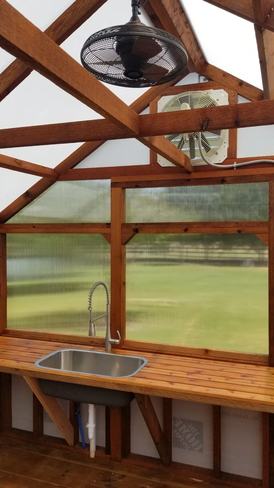 Greenhouse utility sink with a pull-down faucet, a wall-mounted exhaust fan, and a ceiling fan
