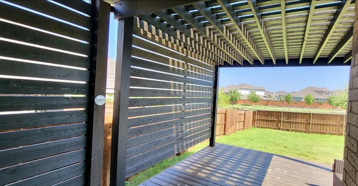 Black stained horizontal slat privacy wall under a pergola